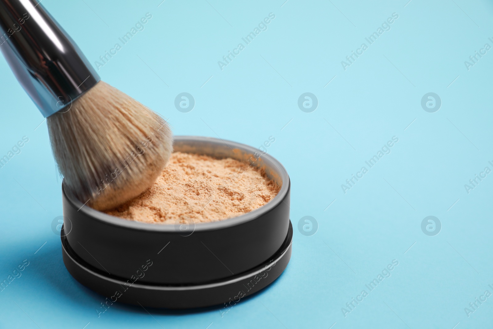 Photo of Applying face powder on brush on light blue background, space for text