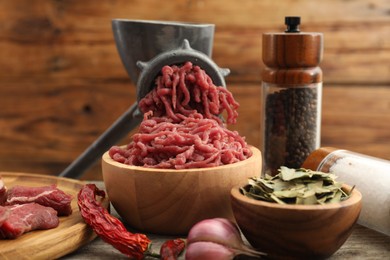 Photo of Manual meat grinder with beef and spices on wooden table, closeup