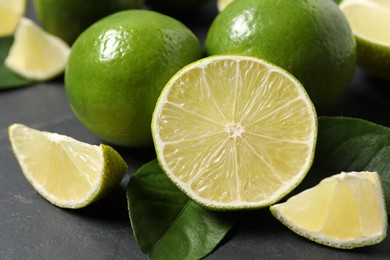 Photo of Fresh ripe limes and leaves on black table, closeup