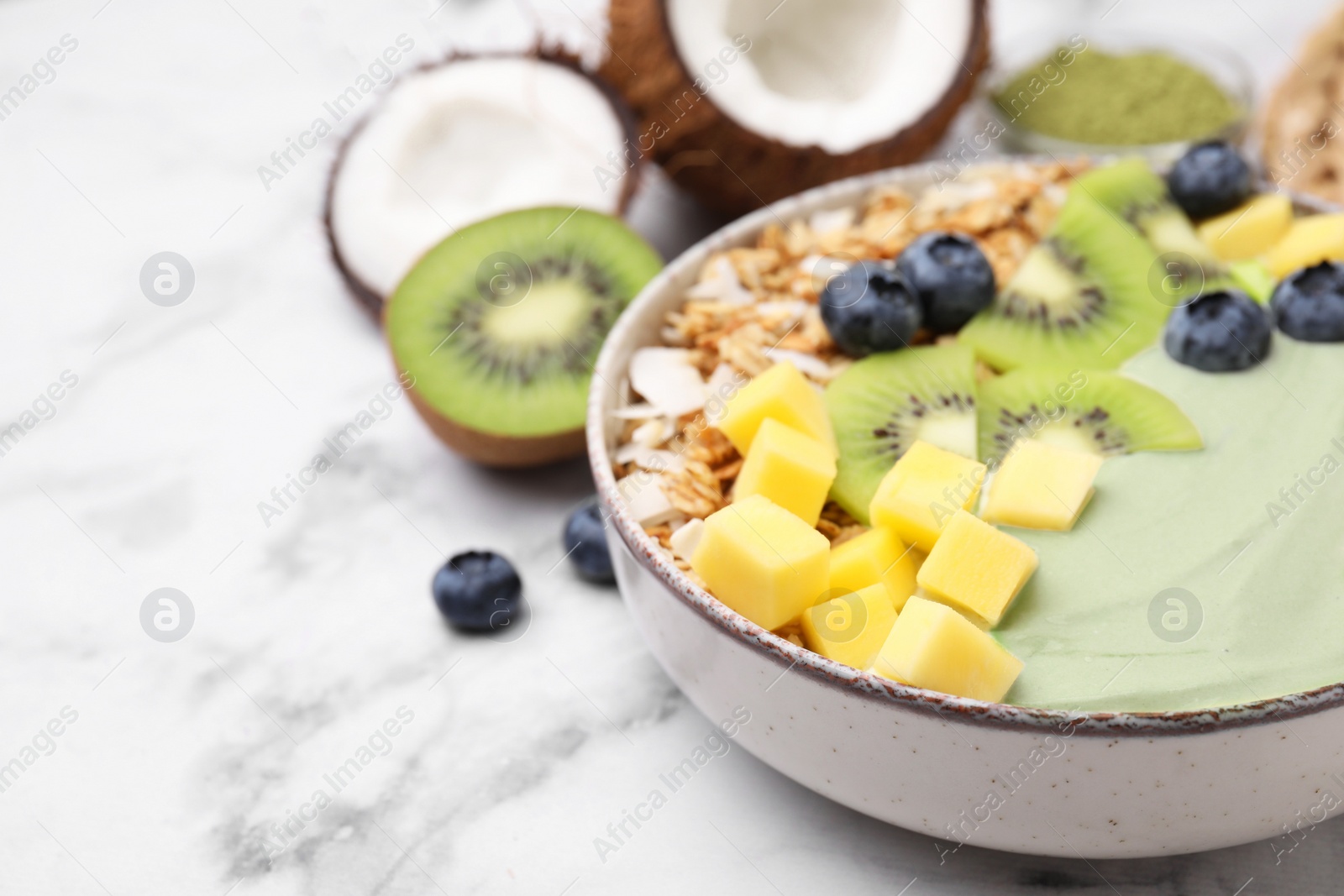 Photo of Tasty matcha smoothie bowl served with fresh fruits and oatmeal on white marble table, closeup with space for text. Healthy breakfast