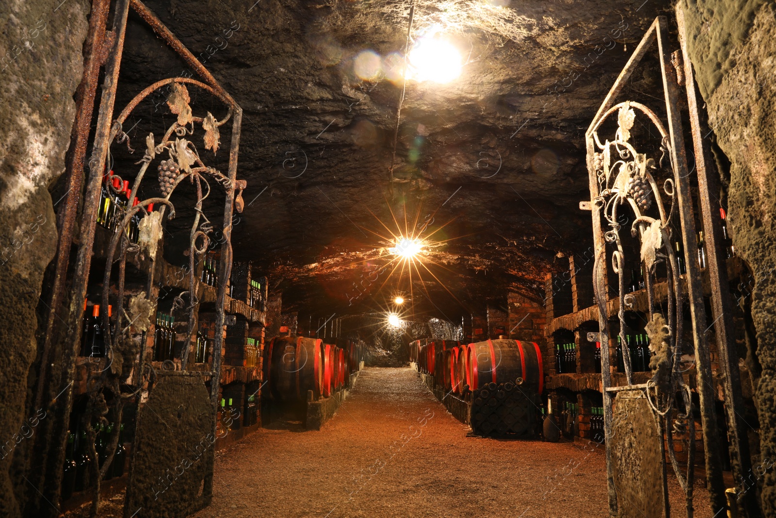 Photo of Bene, Ukraine - June 23, 2023: Many wooden barrels and bottles with alcohol drinks in cellar, low angle view