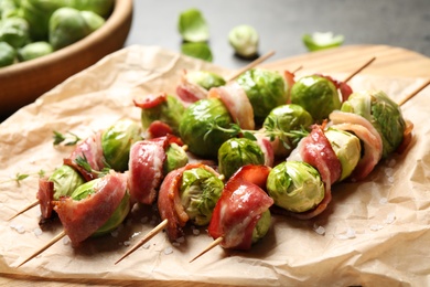 Photo of Skewers with delicious Brussels sprouts and bacon on table