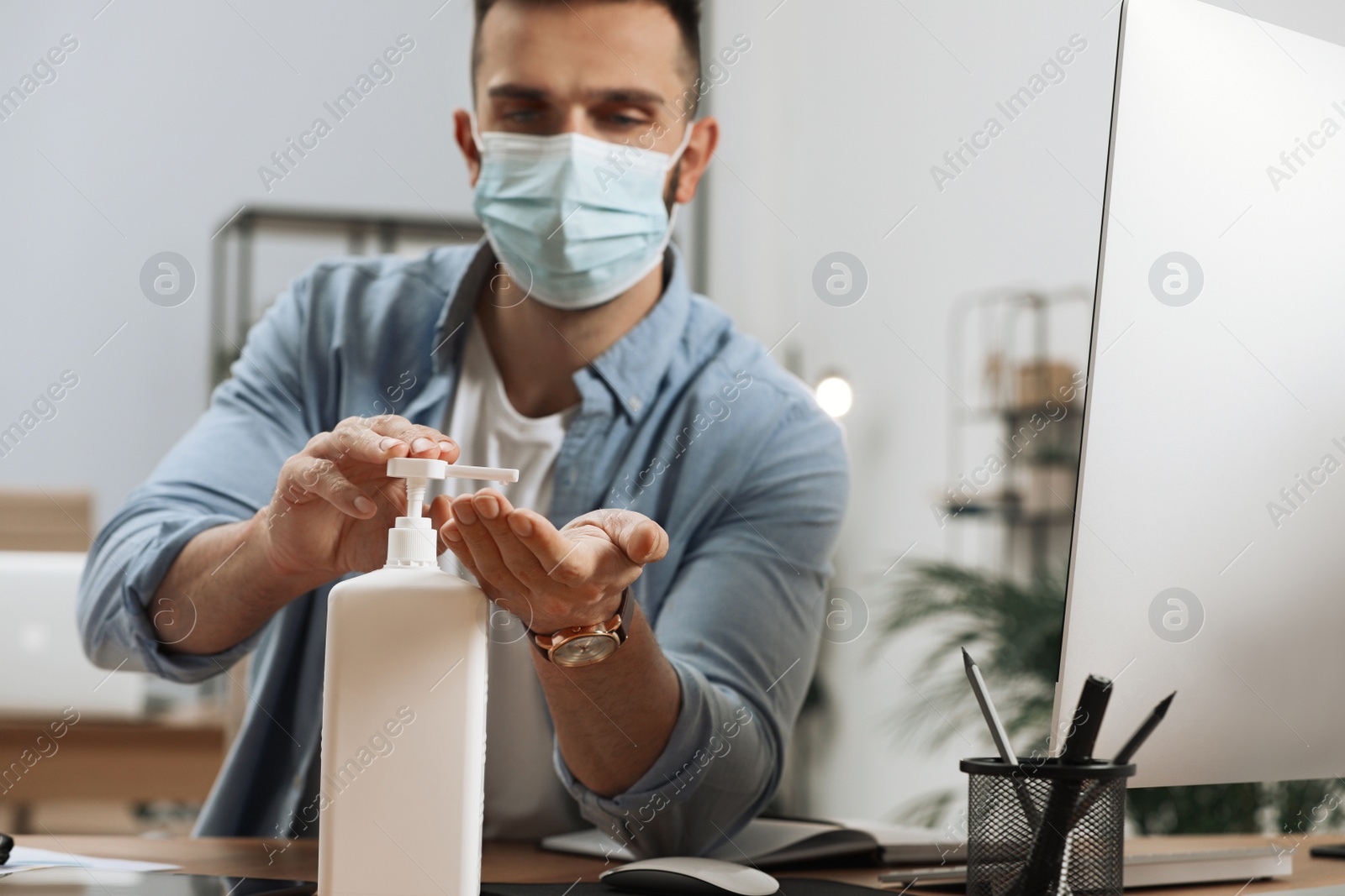 Photo of Man applying sanitizer in office, focus on hands. Personal hygiene during Coronavirus pandemic