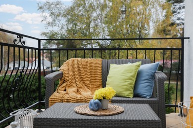 Photo of Colorful pillows, soft blanket and yellow chrysanthemum flowers on rattan garden furniture outdoors