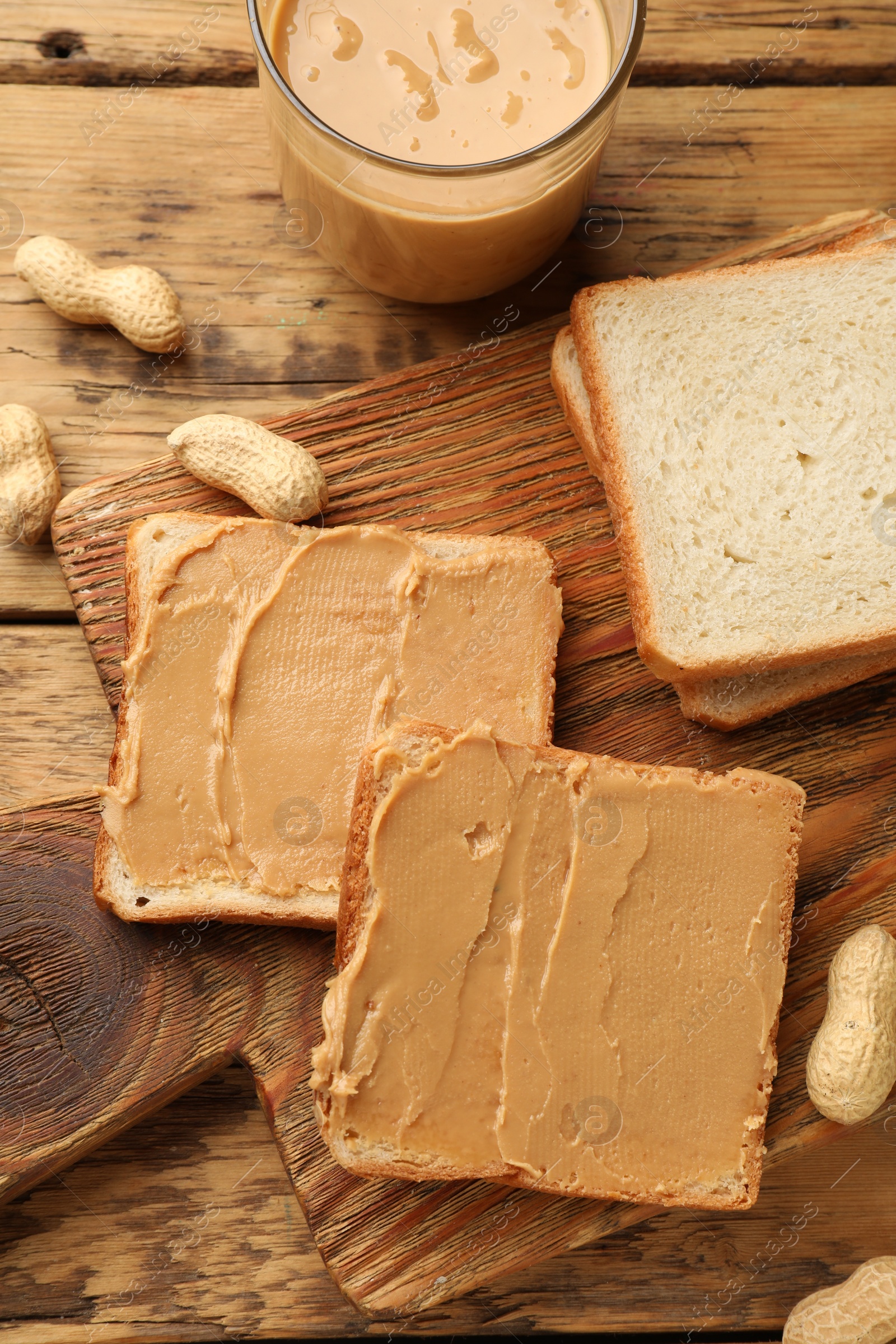 Photo of Tasty peanut butter sandwiches and peanuts on wooden table, flat lay