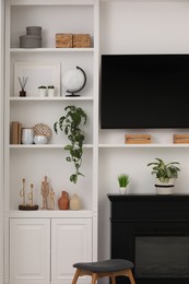 Stylish shelves with decorative elements and houseplants near white wall. Interior design