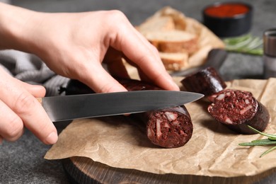 Photo of Woman cutting tasty blood sausage at grey table, closeup