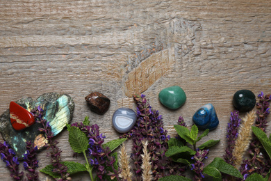 Flat lay composition with different gemstones and healing herbs on wooden table, space for text