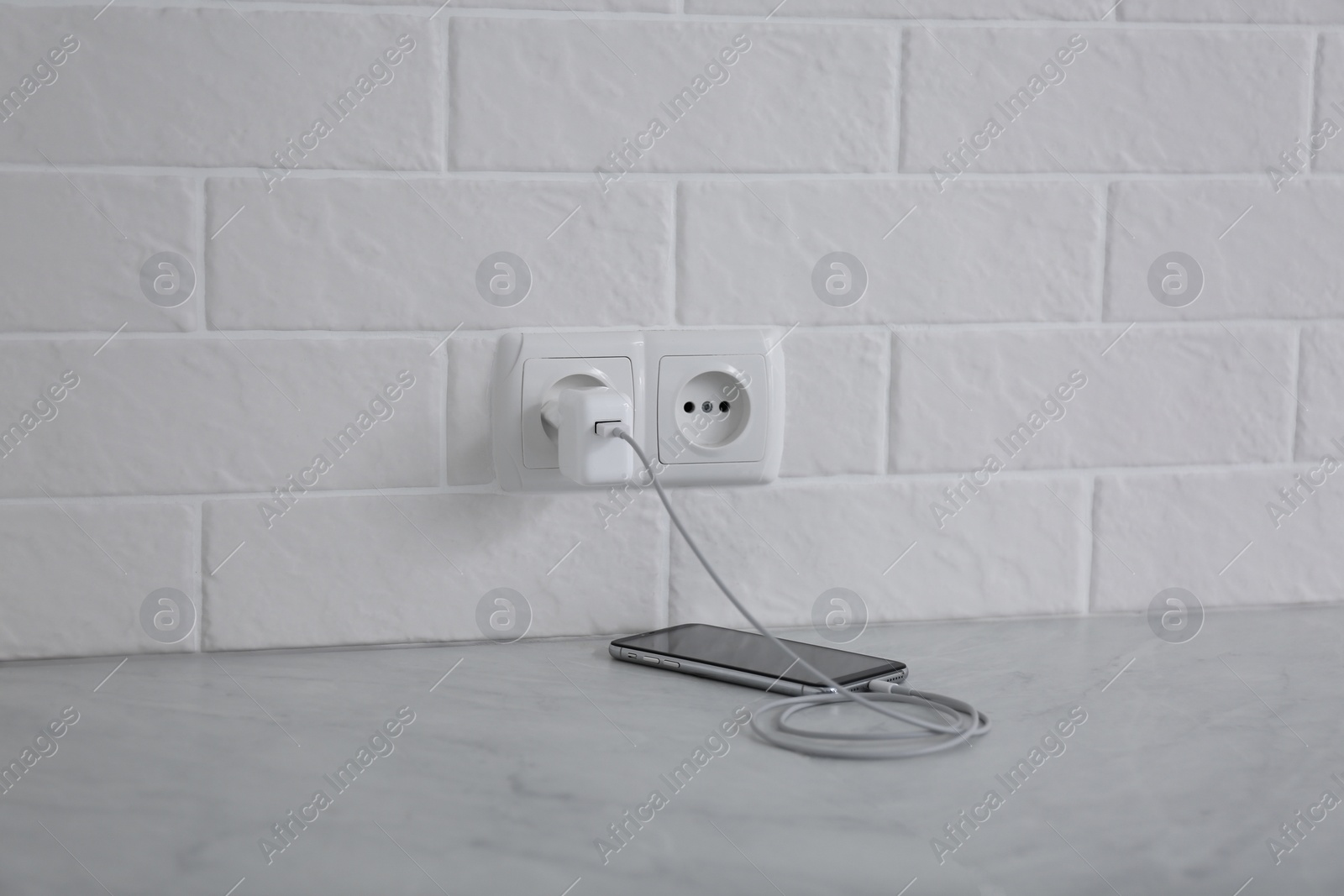 Photo of Modern mobile phone with charger near white brick wall on floor