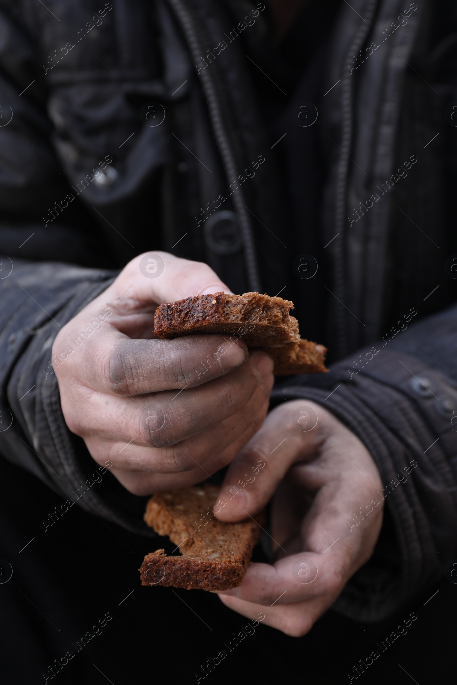 Photo of Poor homeless man holding piece of bread outdoors, closeup