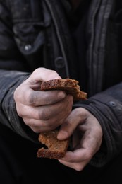 Photo of Poor homeless man holding piece of bread outdoors, closeup