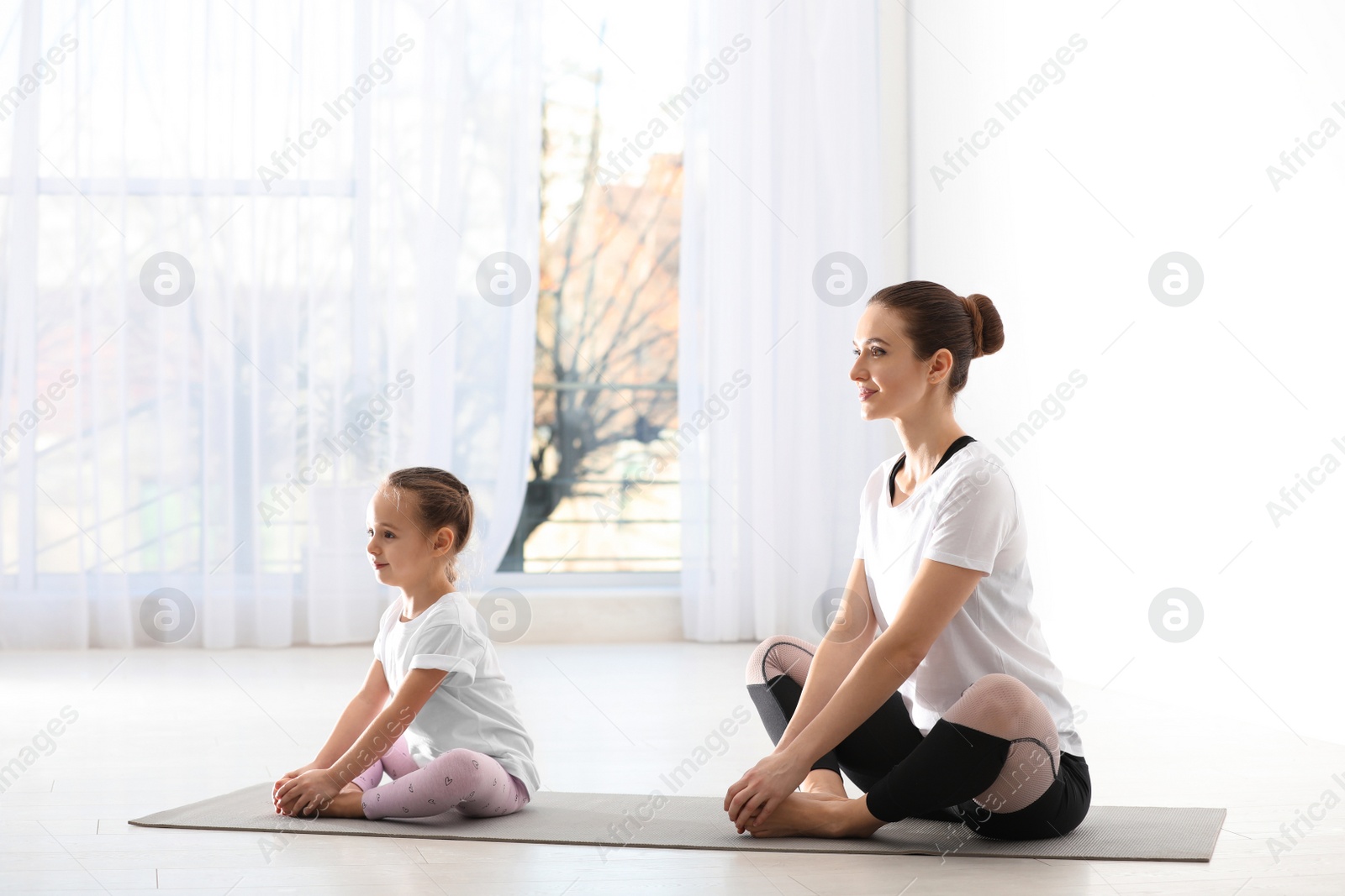 Photo of Young mother with little daughter practicing yoga at home