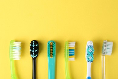 Photo of Different toothbrushes on yellow background, flat lay. Space for text