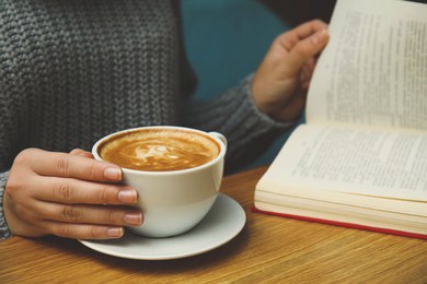 Woman with cup of coffee reading book at table, closeup