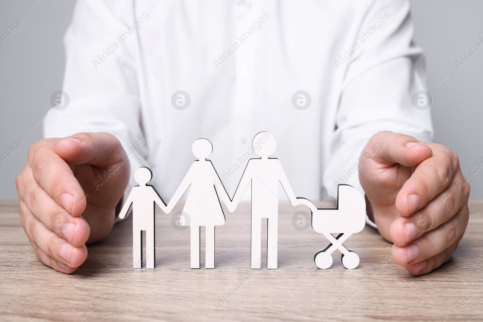 Photo of Man protecting figures of family at wooden table. closeup. Insurance concept