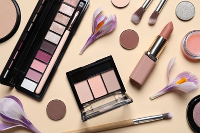 Photo of Flat lay composition with different makeup products and beautiful flowers on beige background