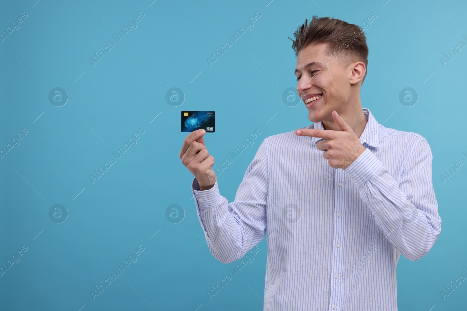 Photo of Happy man pointing at credit card on light blue background. Space for text