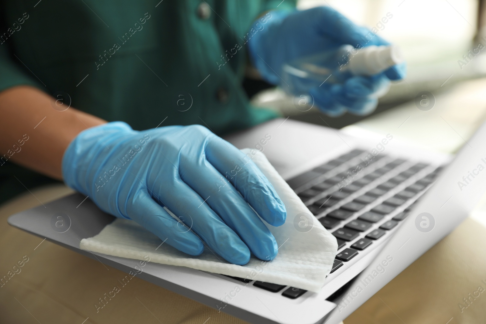 Photo of Woman in latex gloves cleaning laptop with wet wipe indoors, closeup