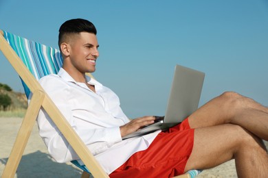 Photo of Happy man working with laptop on beach. Business trip