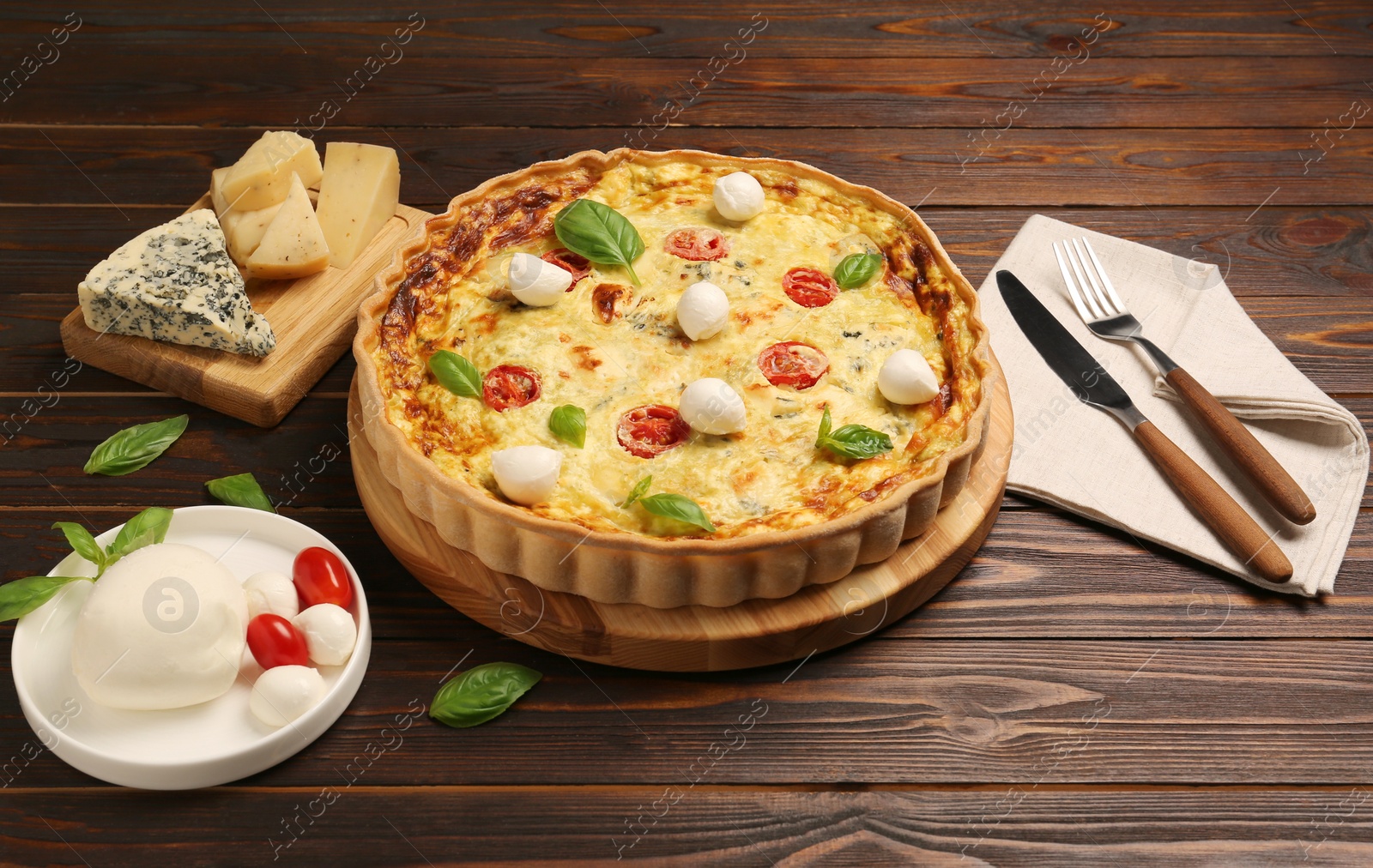 Photo of Delicious quiche with mozzarella cheese, tomatoes and basil on wooden table