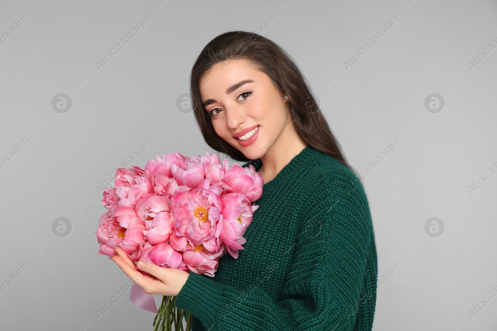 Photo of Beautiful young woman with bouquet of peonies on light grey background