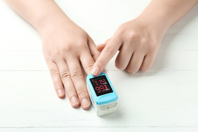 Photo of Woman using fingertip pulse oximeter at white wooden table, closeup