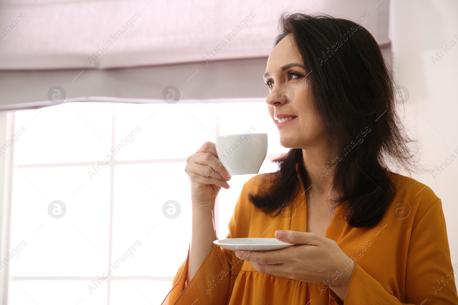 Photo of Beautiful mature woman with cup of coffee at home. Space for text