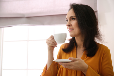 Photo of Beautiful mature woman with cup of coffee at home. Space for text