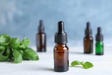 Glass bottle of essential oil and basil on table