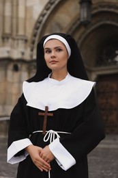 Young nun with Christian cross near building outdoors