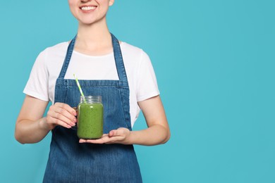 Photo of Woman in denim apron with delicious smoothie on light blue background, closeup. Space for text