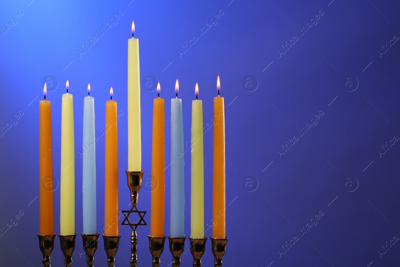 Photo of Hanukkah celebration. Menorah with burning candles on blue background, space for text