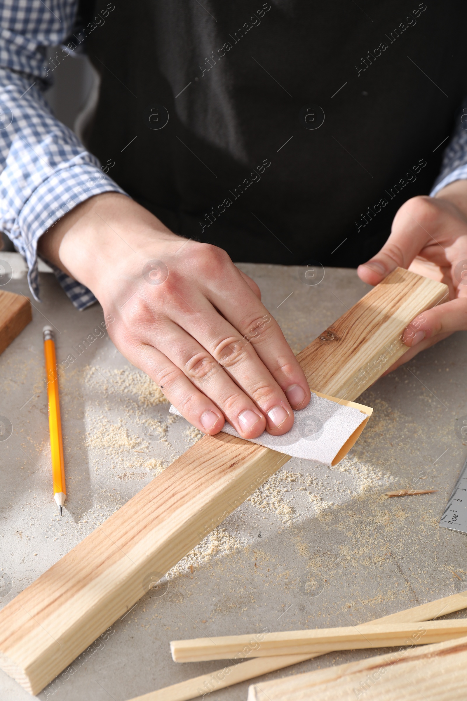 Photo of Man polishing wooden plank with sandpaper at grey table, closeup