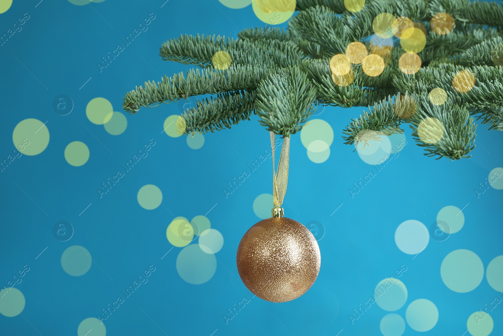 Image of Beautiful Christmas ball hanging on fir tree branch against light blue background. Bokeh effect