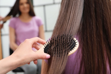 Photo of Woman combing friend's hair with cushion brush indoors, closeup