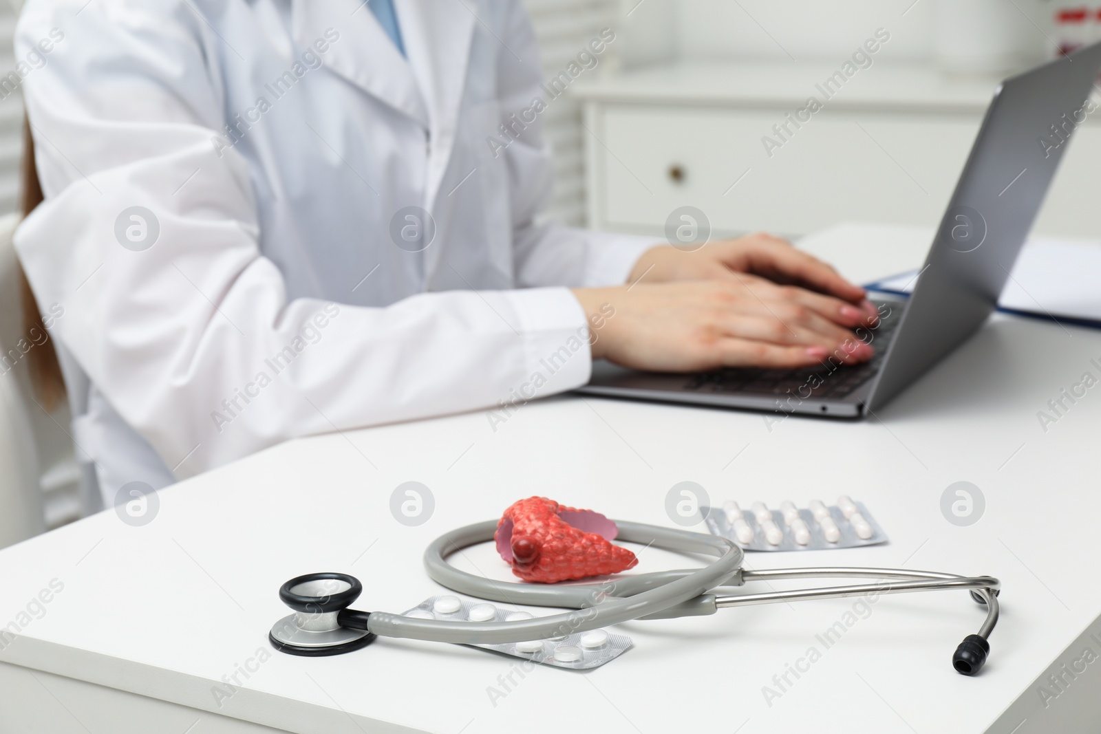 Photo of Endocrinologist working at table, focus on stethoscope and model of thyroid gland