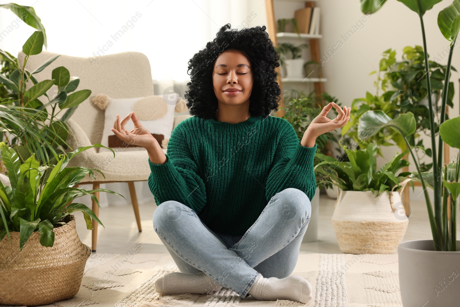 Photo of Relaxing atmosphere. Woman meditating near potted houseplants in room