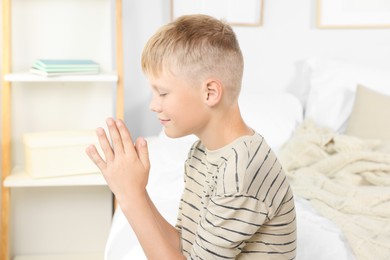 Boy with clasped hands praying on bed at home