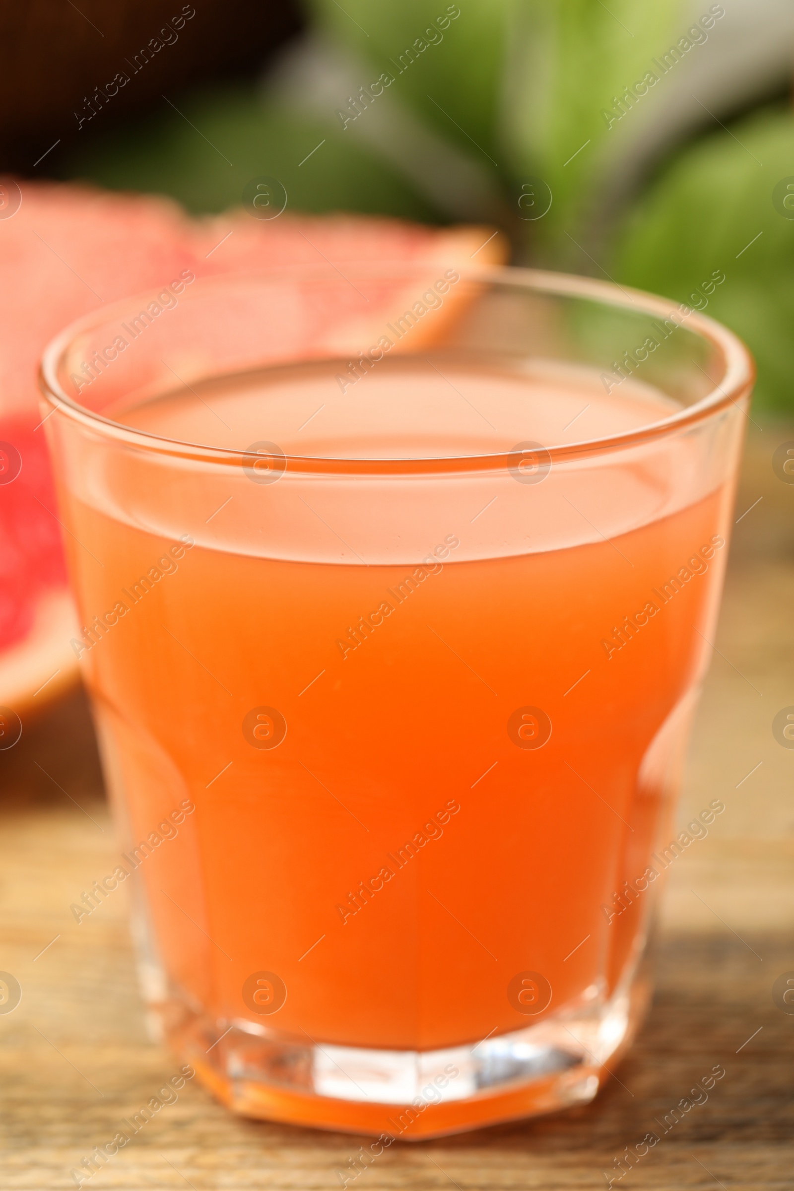 Photo of Glass of delicious grapefruit juice on wooden table against blurred background