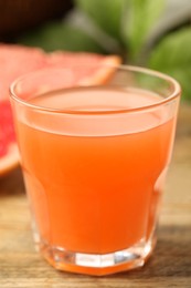 Photo of Glass of delicious grapefruit juice on wooden table against blurred background