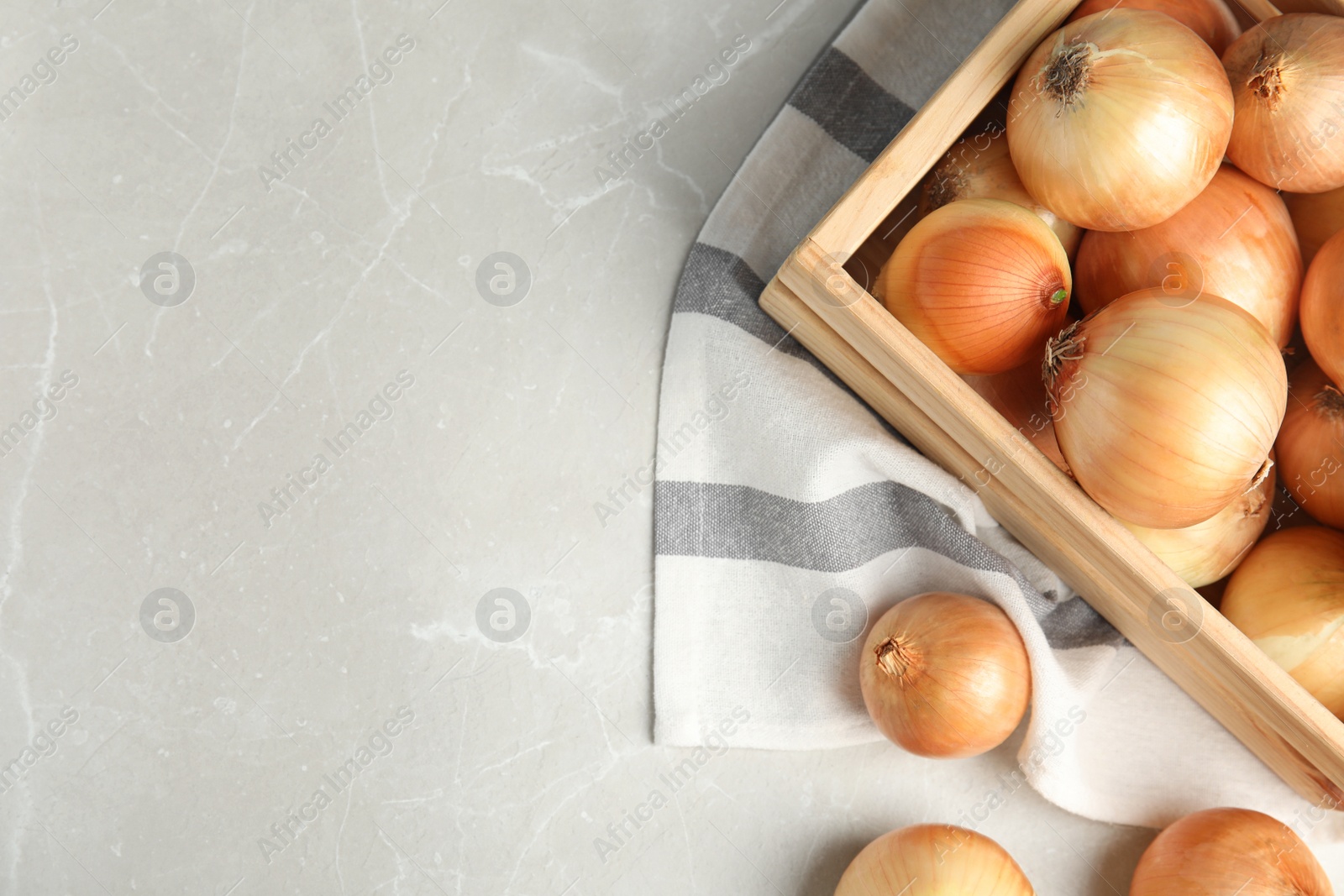 Photo of Wooden crate with ripe onions on grey table, flat lay. Space for text