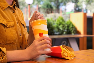 MYKOLAIV, UKRAINE - AUGUST 11, 2021: Woman with cold McDonald's drink and French fries outdoors, closeup