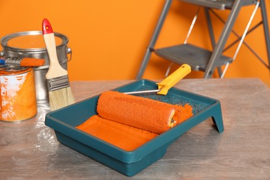 Photo of Tray with orange paint and roller on table