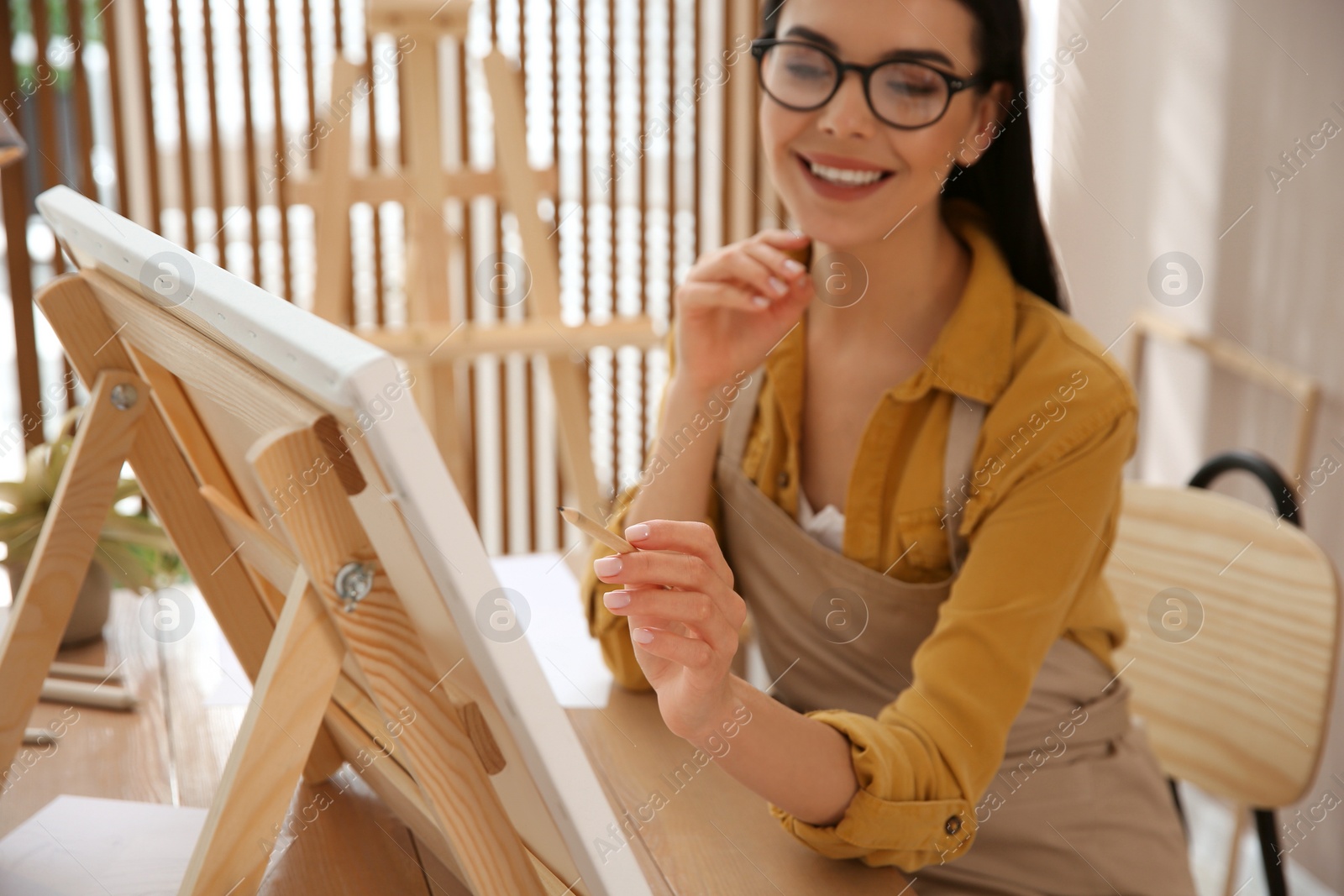 Photo of Young woman drawing on easel with pencil at table indoors