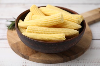 Photo of Tasty fresh yellow baby corns in bowl on white wooden table, closeup