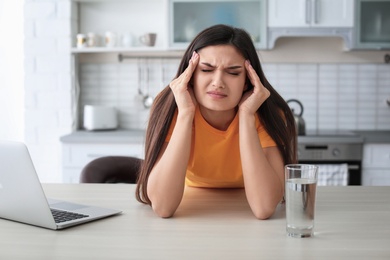 Photo of Young woman suffering from headache in kitchen