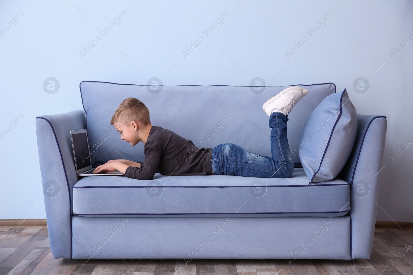 Photo of Cute little boy lying on sofa with laptop, indoors