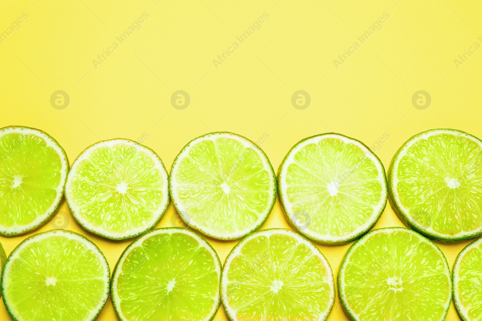 Photo of Juicy fresh lime slices on yellow background, flat lay. Space for text