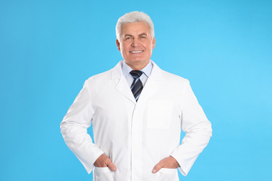 Photo of Happy senior man in lab coat on light blue background