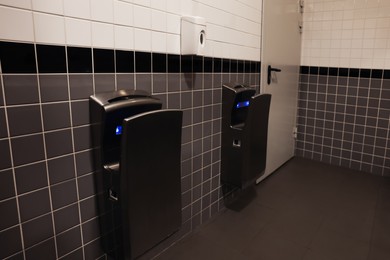 Photo of Modern hand dryers on tiled wall in public toilet